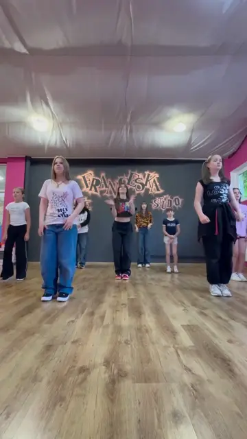 Grupa de K-Pop dansând în fața peretelui cu sigla
